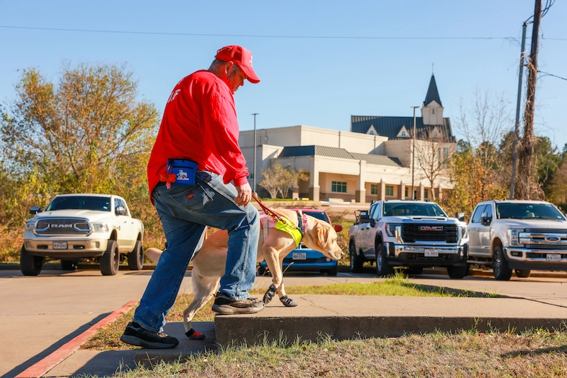 Charles and his guide dog Tango stepping up a curb together. Tango is wearing boots and helping Charles navigate an obstacle